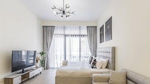 A modern hotel room with a large bed, a sofa, a TV, and a dining area. - Relaxing Studio Retreat in Vibrant Meydan City, (Dubai)