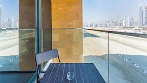 A balcony with a glass partition, a chair, and a table. - Relaxing Studio Retreat in Vibrant Meydan City, (Dubai)