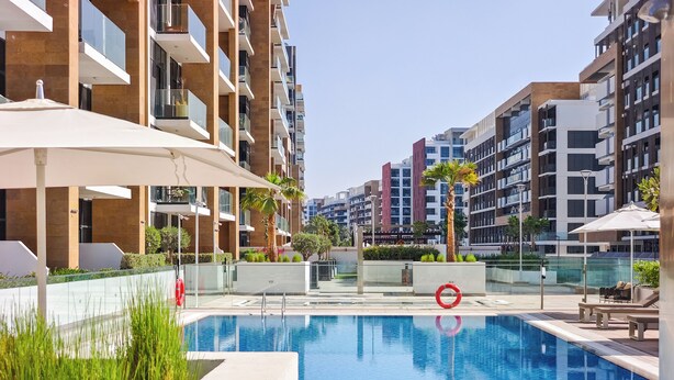 A modern residential building with a swimming pool, outdoor seating, and a clear sky. - Relaxing Studio Retreat in Vibrant Meydan City, (Dubai)