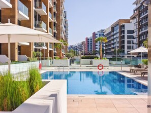 Ein modernes Wohngebäude mit Schwimmbad, Sitzgelegenheiten im Freien und blauem Himmel.