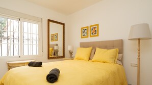 A room with a bed, a bedside table, a lamp, and a window with a view of greenery. - Charming Coastal Home (Marbella)