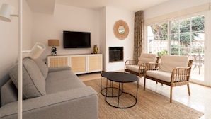 A modern living room with a grey sofa, two armchairs, a coffee table, a TV, and a fireplace. - Charming Coastal Home (Marbella)