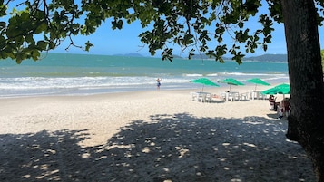 Una playa con vista despejada al océano, una persona caminando y varios sombrillas verdes y sillas blancas.