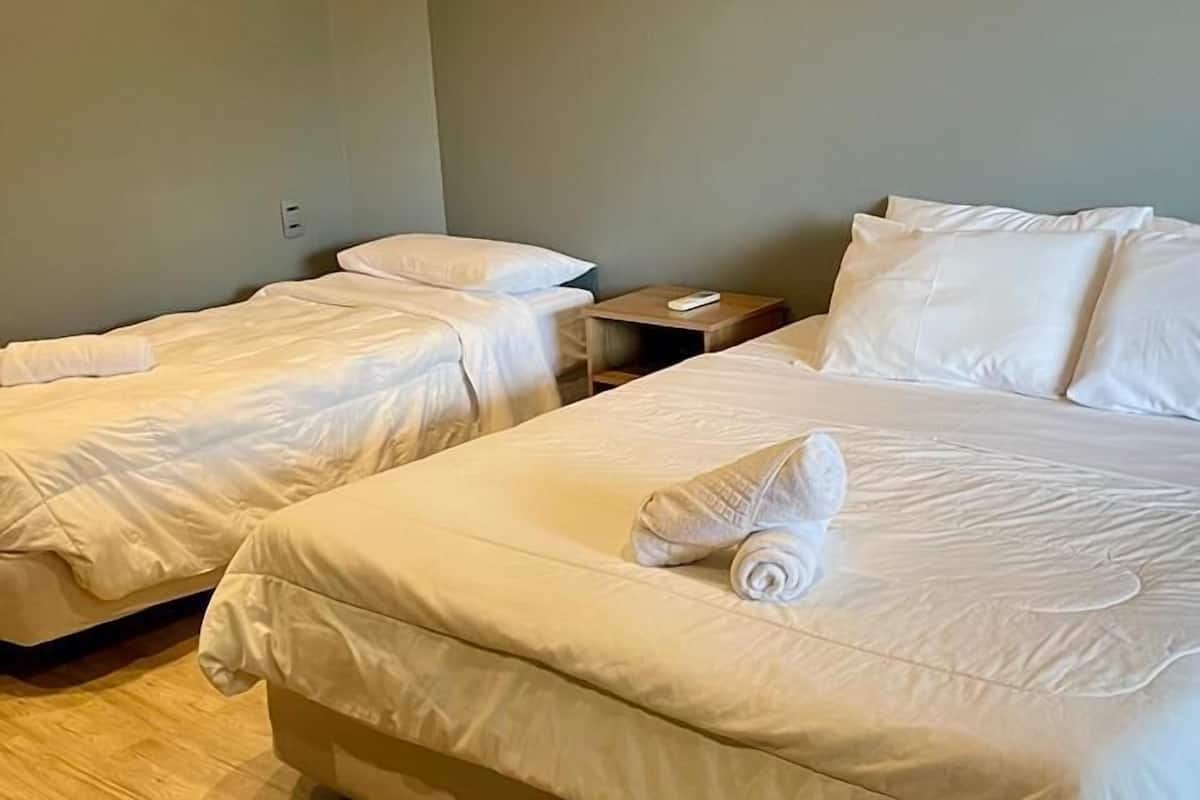A hotel room with two single beds, a wooden floor, and a small bedside table with a remote control.