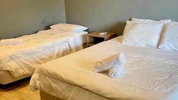 Quarto de hotel com duas camas de solteiro, piso de madeira e uma pequena mesa de cabeceira com controle remoto.
