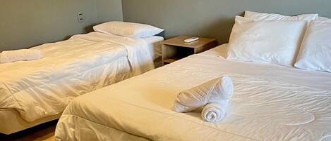 Una habitación de hotel con dos camas individuales, piso de madera y una mesita de noche pequeña con un control remoto.