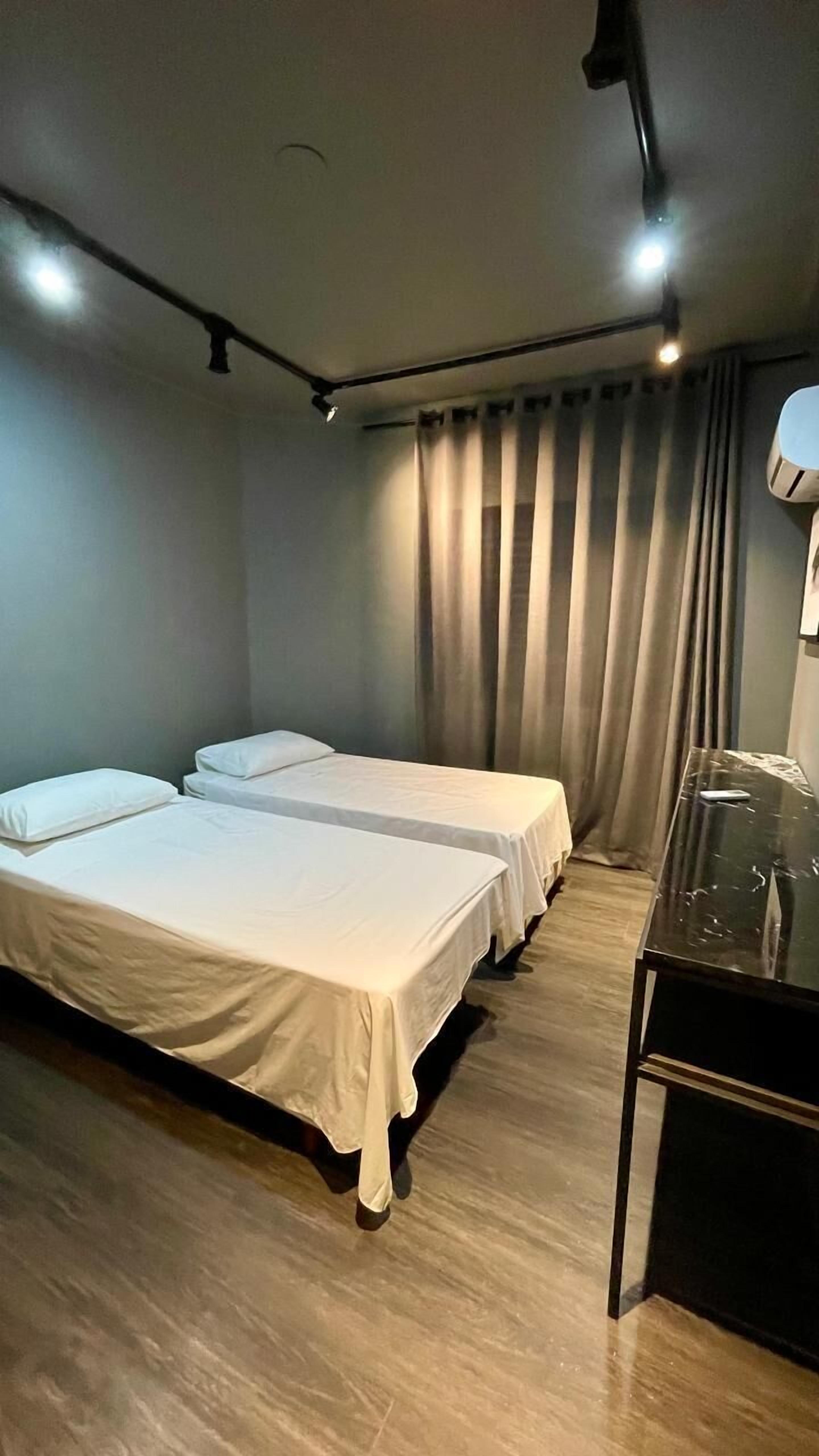 A hotel room with two single beds, a desk with a lamp, and a curtain-covered window.
