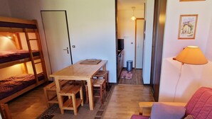 Een kleine kamer met stapelbedden, een houten tafel, een kleine bank en een lamp.