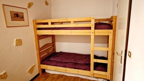 Een stapelbed met houten frame en paars beddengoed, een deur met hendel en een ingelijst kunstwerk aan de muur.