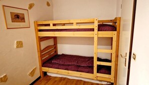 Una cama litera con estructura de madera y ropa de cama púrpura, una puerta con picaporte y un cuadro enmarcado en la pared.
