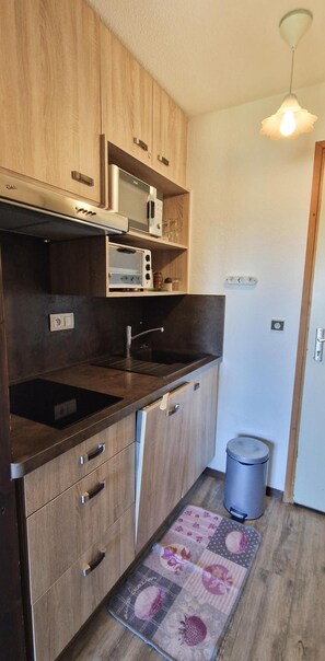 A compact kitchen with wooden cabinets, a microwave, a toaster, and a trash bin. - 50m from ski slopes, 1st floor, balcony, tv, 26m², Montalbert (La Plagne)