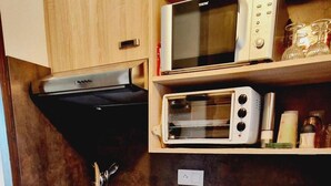 Een compacte keuken met houten kastjes, een magnetron, een broodrooster en een spoelbak.
