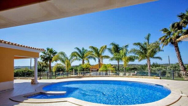 A swimming pool with a tiled deck, surrounded by palm trees and a clear sky. - Quinta do Sol in Guia (Albufeira)
