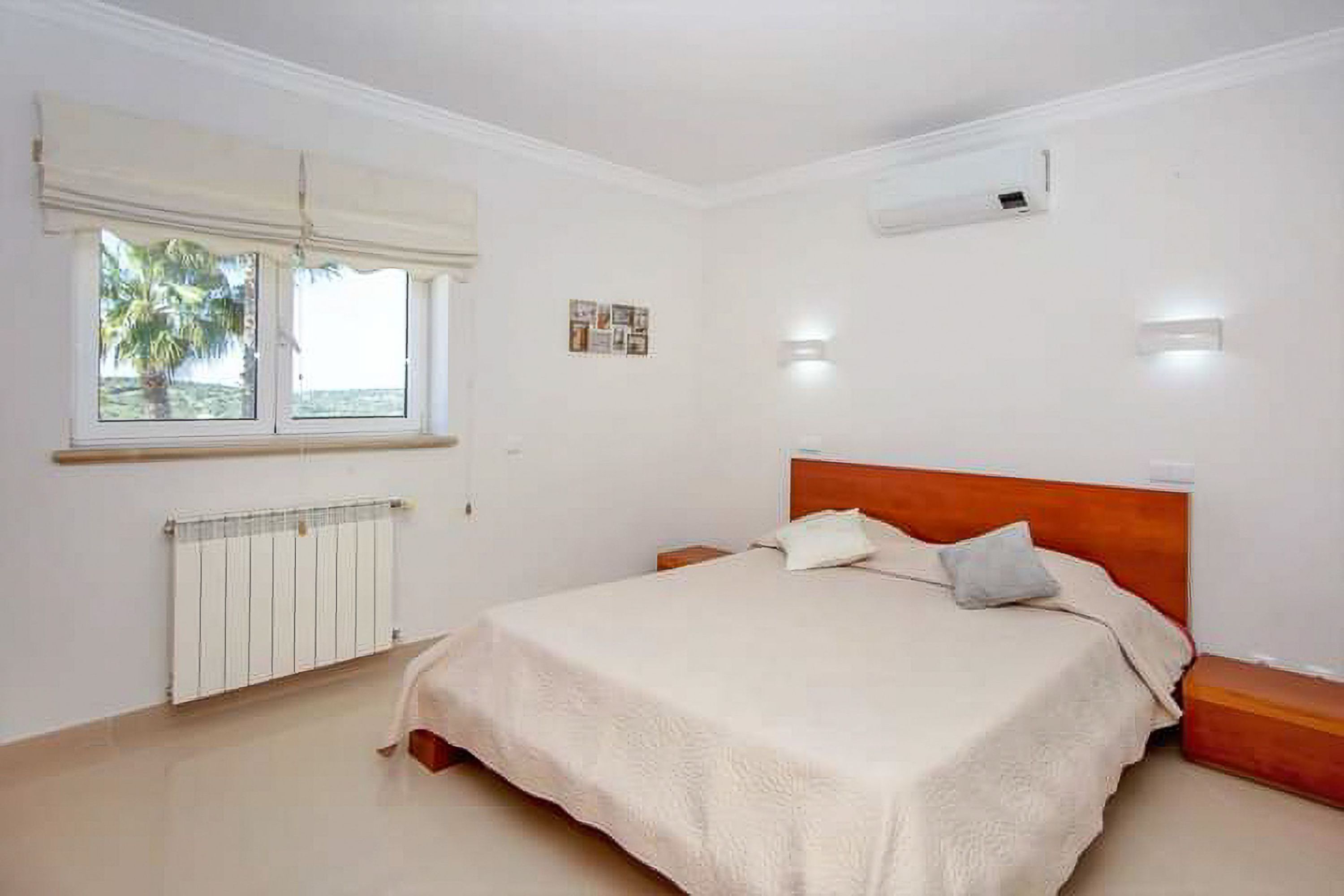 A bedroom with a bed, a window with blinds, a radiator, and wall-mounted lights.