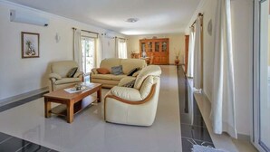 A spacious living room with a sofa, armchair, and coffee table. A wooden cabinet is visible in the background. - Quinta do Sol in Guia (Albufeira)
