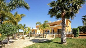A yellow villa with a spacious patio, palm trees, and a clear blue sky. - Quinta do Sol in Guia (Albufeira)