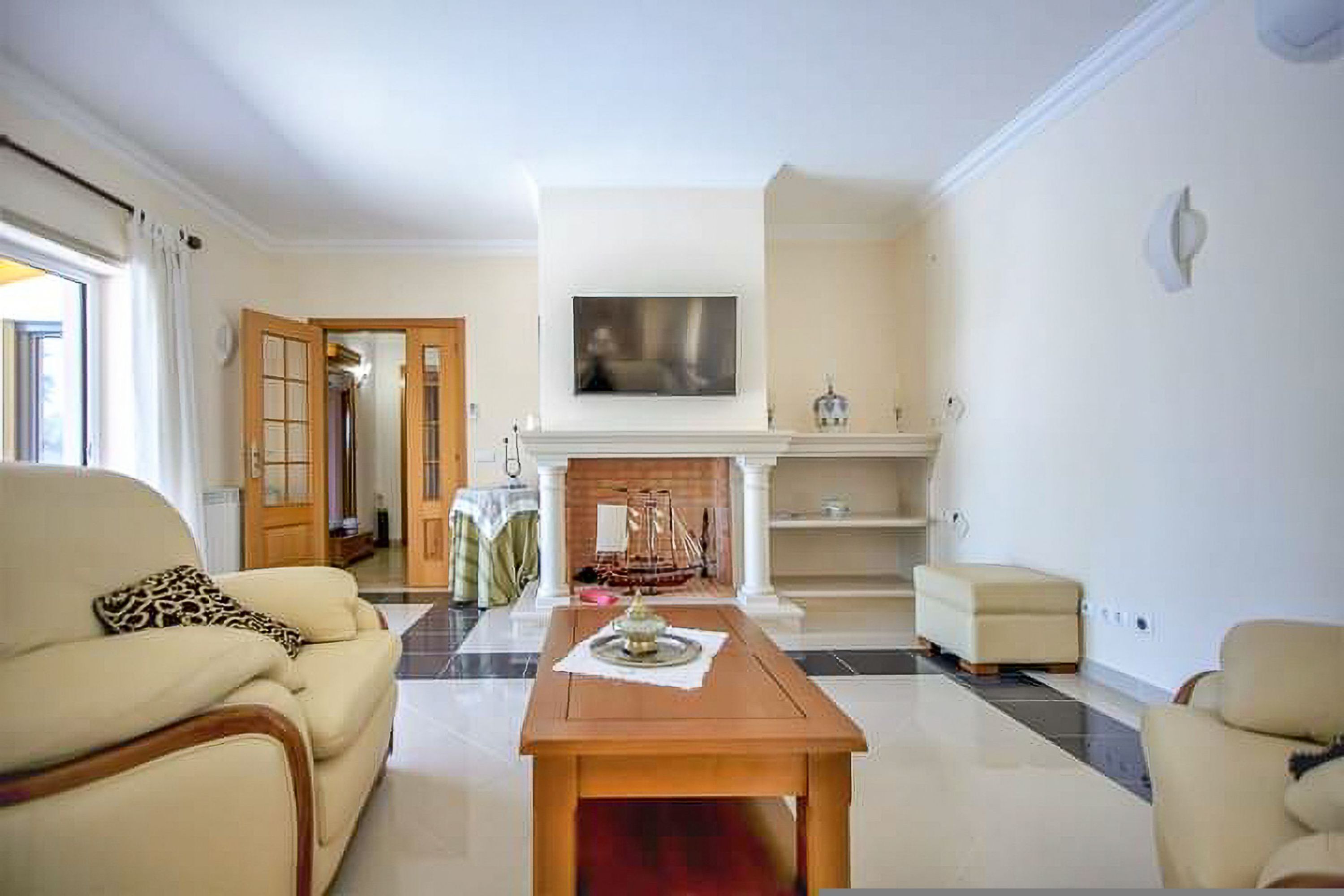 A living room with a fireplace, a sofa, a coffee table, and a television mounted above the fireplace.