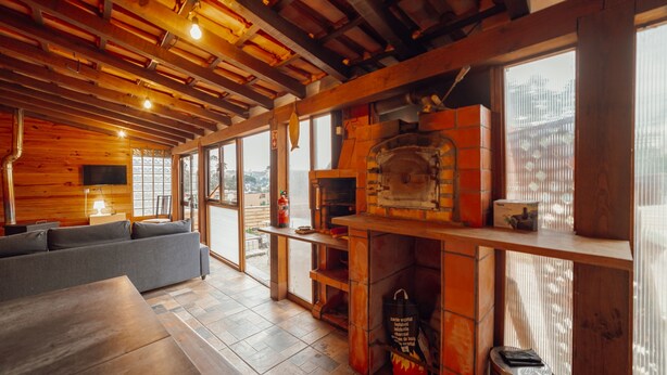 A cozy interior with a wooden ceiling, a fireplace, a sofa, and a dining table.