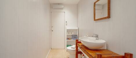 A bathroom with a wooden vanity, white sink, and a mirror. There is a toilet and a shelf with toiletries.