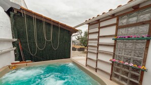 A hot tub with a green wall and wooden beams, a window with a flower shelf, and a clear sky.