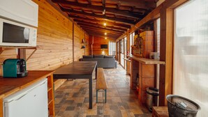 A wooden cabin interior with a kitchen area, a dining table, and a sofa.