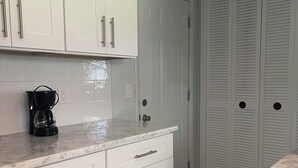 A kitchen with white cabinets, a marble countertop, and a coffee maker. - Enjoy SWFL (Fort Myers)