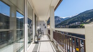 A balcony with a view of snow-capped mountains, a table with chairs, and a glass railing. - Spacious Apartment With Mountain View (Bad Gastein)