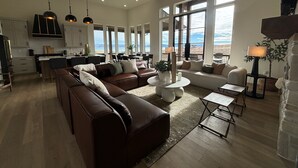 A spacious living area with a large brown leather sofa, a coffee table, and a dining area with a view of the mountains.