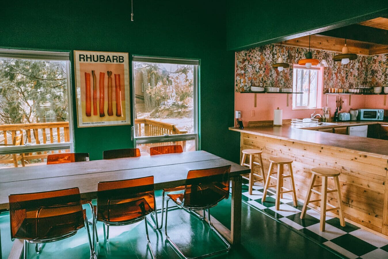 Un restaurante con mesa y sillas de madera, una zona de cocina con mostrador y taburetes, y un cartel de ruibarbo en la pared.