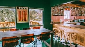 Un restaurante con mesa y sillas de madera, una zona de cocina con mostrador y taburetes, y un cartel de ruibarbo en la pared.