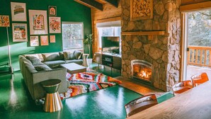 Een gezellige woonkamer met een stenen openhaard, groene wanden en een groot raam met uitzicht op een terras.