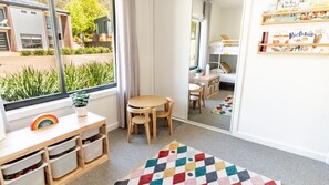 Une chambre d’enfant avec une fenêtre, une petite table et des chaises, des boîtes de rangement et un tapis coloré.