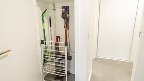 Ein Flur mit einem Metallregal, auf dem Reinigungsmittel, ein Staubsauger und ein Wischmopp stehen.