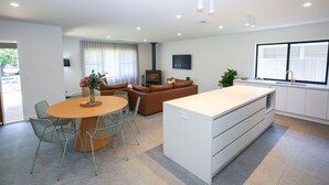 A modern living room with a sofa, a coffee table, and a TV. There's a kitchen area with a sink and cabinets. - Manning Retreat - your family haven on Gavan St (Bright)
