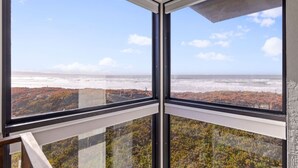 Habitación con ventanas amplias que ofrecen vista al océano y a una zona boscosa.