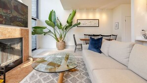 Una sala de estar moderna con una mesa de centro de vidrio, un sofá, una chimenea y una zona de comedor con sillas y una mesa.