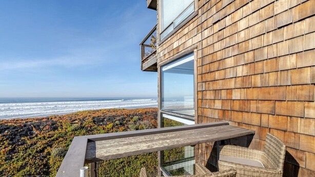 Un balcón con vista al océano, fachada de madera y mobiliario de mimbre.