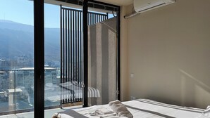 Una habitación de hotel moderna con un gran ventanal, una cama, una lámpara colgante y un equipo de aire acondicionado.