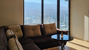 Una sala de estar moderna con un amplio sofá modular, una mesa de centro redonda y vistas de un paisaje urbano a través de ventanas de piso a techo.