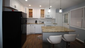 A modern kitchen with white cabinets, a black refrigerator, granite countertops, and two bar stools. - Beautiful Single Family Home (Evesham)