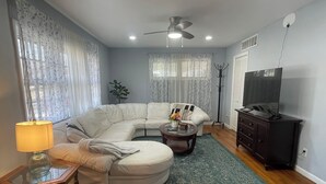 A living room with a sectional sofa, a glass coffee table, a TV stand, and a ceiling fan. - Beautiful Single Family Home (Evesham)