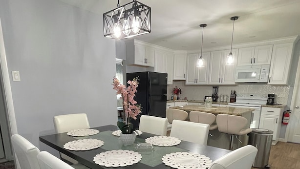 A dining area with a rectangular table, white chairs, and a black chandelier. - Beautiful Single Family Home (Evesham)