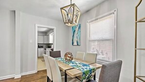 Een eethoek met een houten tafel, witte stoelen en een geometrisch hanglamp.