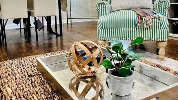 Een woonkamer met een gestreepte fauteuil, een bijzettafel met een decoratieve bol, en een boekenkast met decoratieve objecten.