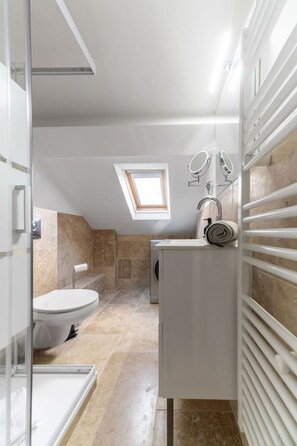 Ein modernes Badezimmer mit Dachfenster, Toilette, Waschmaschine und Handtuchhalter.