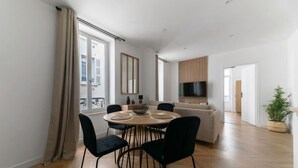 A modern living room with a round dining table, black chairs, a sofa, and a TV mounted on the wall.
