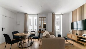 A modern living room with a sofa, dining table, chairs, and a TV.