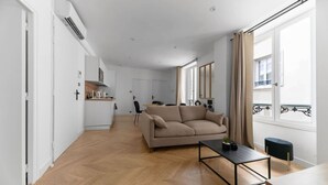 A modern living room with a sofa, a coffee table, and a view of the kitchen and balcony.