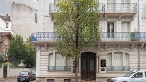 Ein mehrstöckiges Gebäude mit einem zentralen Eingang, Balkonen und einem Baum davor.