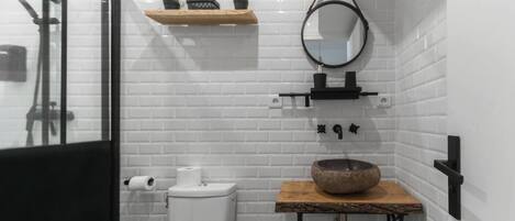 Un baño moderno con azulejos blancos tipo metro, un lavabo negro con una pila de piedra, un espejo y un estante con plantas.